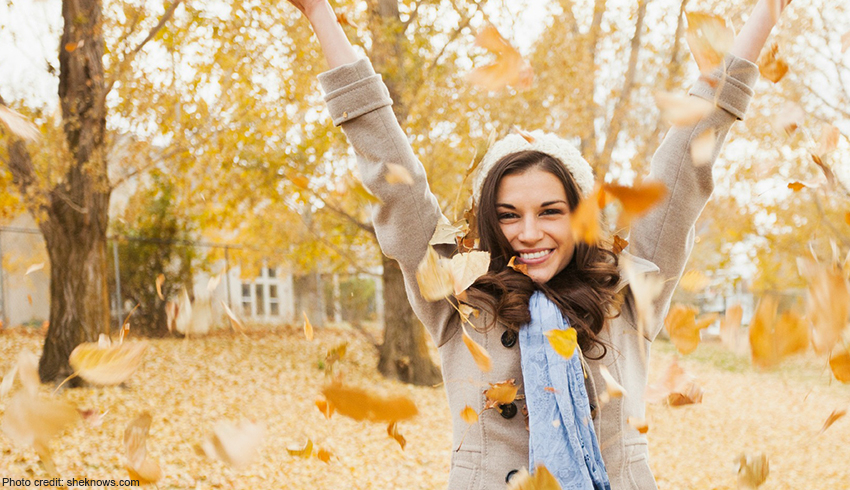 A woman throw fall leaves into the air as she stands outside